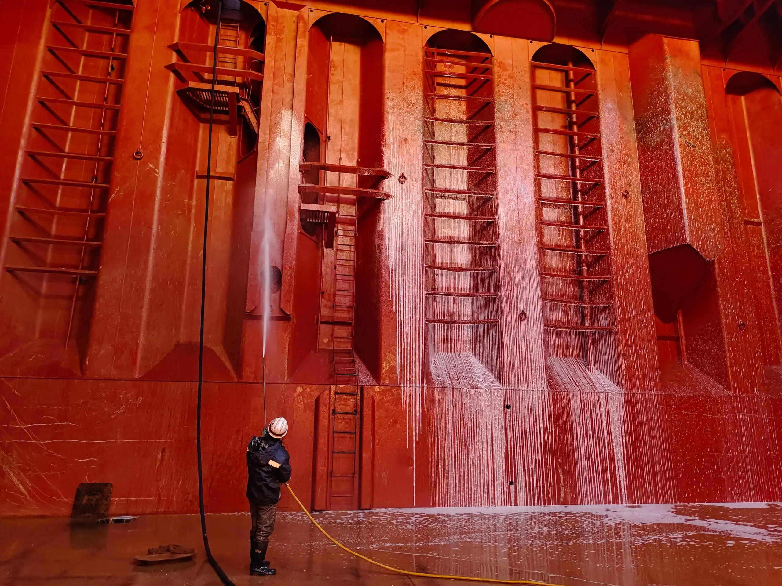 Worker with a high-pressure lance washing down the ribbed bulkhead of a bulk carrier hold.